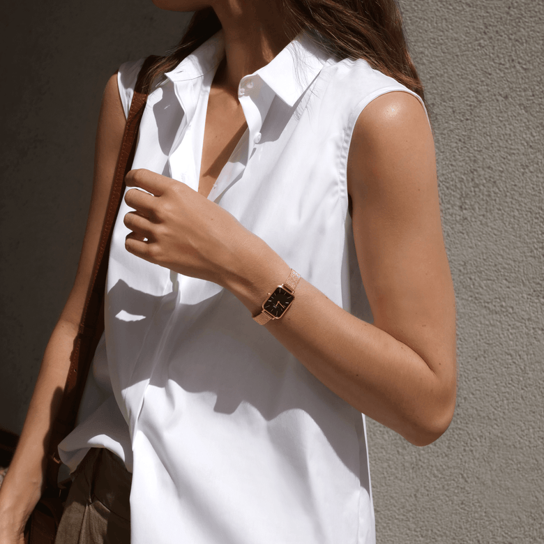 A woman wearing the Quadro Pressed Melrose Black Rose Gold watch with a slim rectangular black dial and rose gold mesh bracelet, styled with a sleeveless white shirt for a polished everyday look.