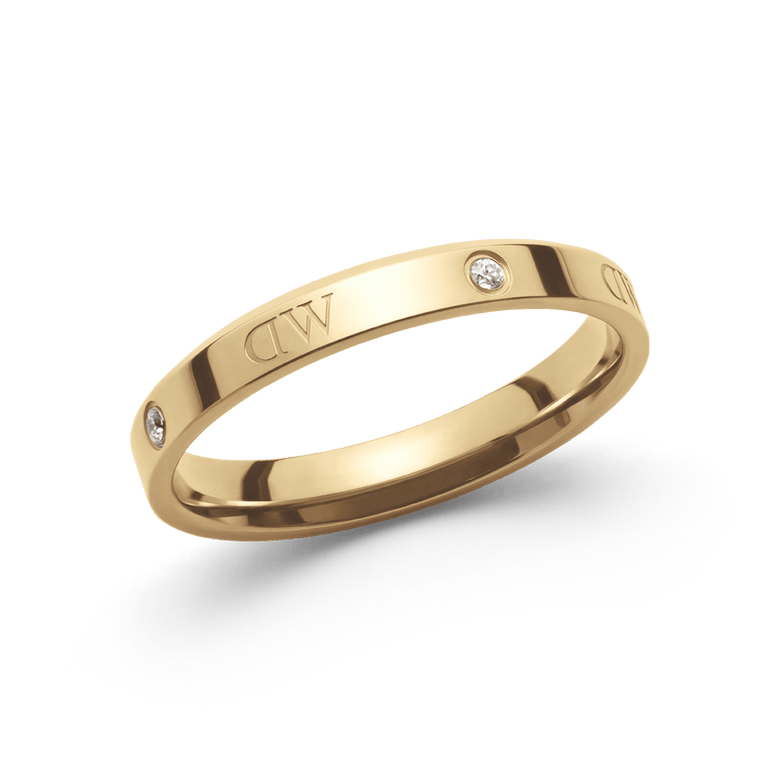 A slim gold ring with a polished finish, featuring engraved branding and sparkling crystal accents spaced evenly around the band.