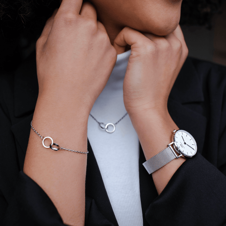 Woman wearing the Elan Unity Bracelet Silver with two interlocking rings on a slim chain, styled alongside a matching necklace and silver mesh watch for a coordinated, elegant look.
