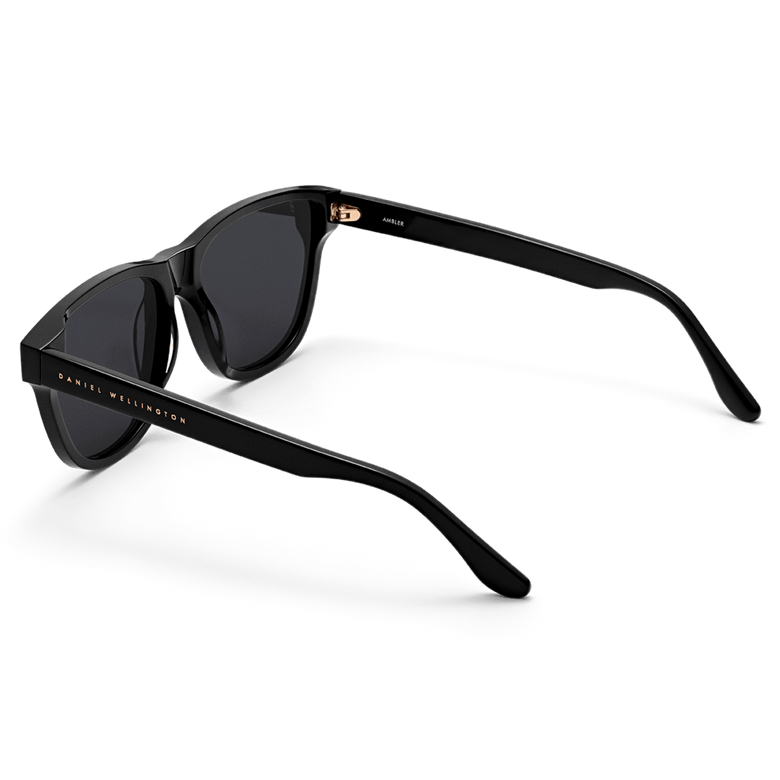 Ambler Bio-Acetate Black sunglasses with a modern classic shape, featuring a glossy black Italian bio-acetate frame, dark UV400 lenses, and the Daniel Wellington logo on the arm.