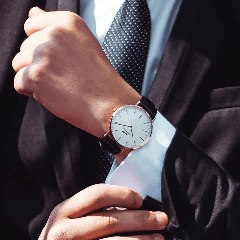 A man in a suit wears the Classic Sheffield Rose Gold watch, featuring a slim rose gold case, minimalist white dial, and black leather strap, styled for a polished business look.