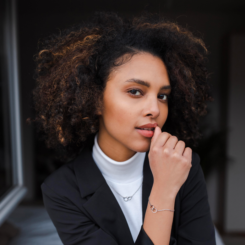 Elan Unity Bracelet Silver worn on the wrist, paired with a matching necklace and styled with a black blazer and white turtleneck for a sophisticated, modern look.