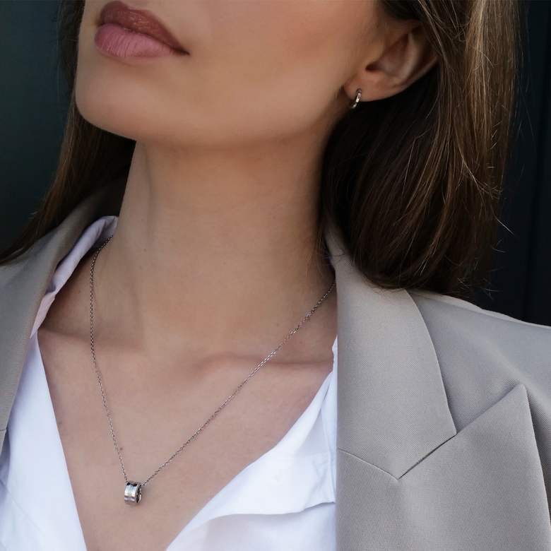 A woman wearing the Elan Necklace Silver, featuring a polished silver ring pendant on a fine chain, styled with a white blouse and beige blazer for a sophisticated, everyday look.